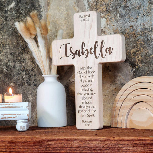 Wooden cross with engraved name and text, placed on a wooden surface with decorative elements.
